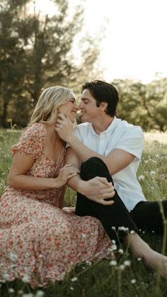 a man and woman are sitting in the grass with their heads touching each other's noses