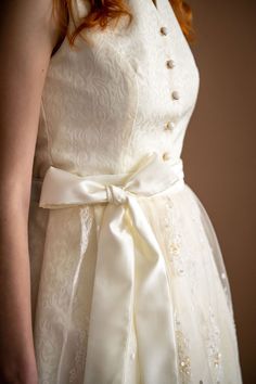 This breathtaking ivory bridal dirndl is a true masterpiece. Crafted from luxurious Jacquard satin fabric, it exudes elegance and sophistication. The bodice is a tailored fit with high collar and gentle v-neckline. The real showstopper, however, is the beaded and embroidered lace apron that adorns the front of the skirt. This intricately detailed apron with delicate lace and beading that shimmers and sparkles in the light. The pearlescent buttons add a touch of glamour to the design. Overall, this ivory bridal dirndl is a work of art that is sure to make any bride feel like royalty on her special day. Ivory jacquard satin medium-length bridal dirndl Pleated skirt length is 26" from the waist to the hemline High collar neckline with gold and pearlescent buttons 2 Skirt pockets Ivory Beaded Dirndl Lace, Bridal Dirndl, Wedding Dirndl, Lace Apron, Skirt Pockets, Ivory Bridal, Ivory Wedding, Congo Kinshasa, Plus Size Wedding