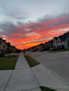 the sun is setting over some houses in this suburban area with grass on both sides