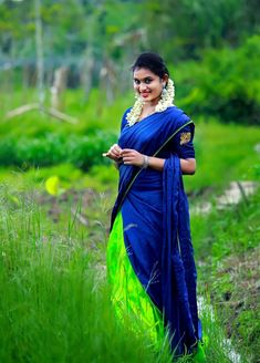 a woman in a blue and green sari standing in the grass with her hand on her hip