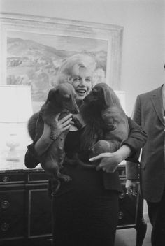 a woman holding a dog in her arms while standing next to a man wearing a suit and tie