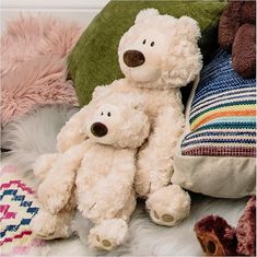 two white teddy bears sitting next to each other on a bed with pillows and blankets