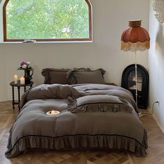 a large bed sitting under a window next to a table with a lamp on it