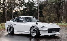 a white sports car parked in front of trees on a wet parking lot with no one around