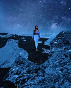 a woman is walking in the middle of an icy field at night with stars above her