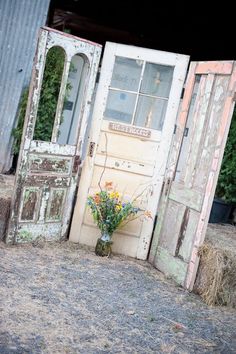 an old door is open and flowers are in the vase next to it on top of hay bales