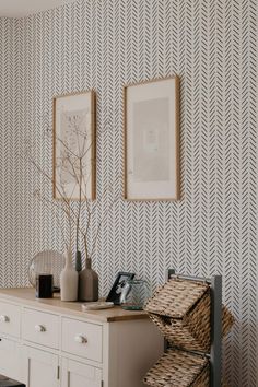 a white dresser sitting next to a wall with two pictures above it and a basket on top of it