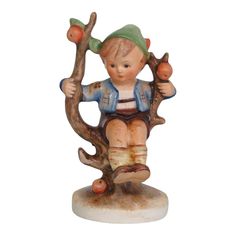 a figurine of a little boy sitting on a tree branch holding an apple