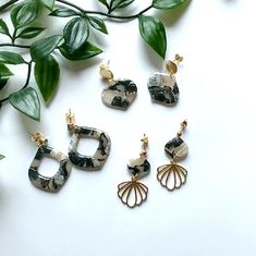 three pairs of earrings sitting on top of a white table next to green plants and leaves