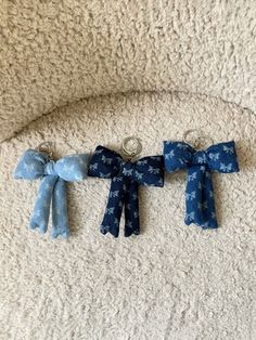 three blue bows are hanging on a white carpeted wall, one is tied to a metal hook