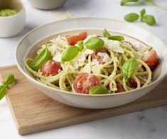 a white bowl filled with pasta and tomatoes on top of a wooden cutting board next to two cups