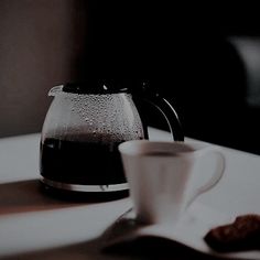 a coffee pot sitting on top of a white table next to a cup filled with liquid