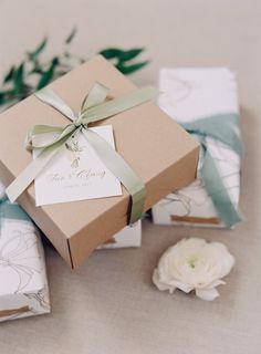 two wrapped gift boxes sitting on top of each other next to flowers and greenery