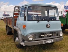 an old truck is parked in the grass with other trucks behind it and people standing around