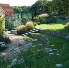 an outdoor garden with stone walls and steps leading to the back yard, surrounded by lush green grass