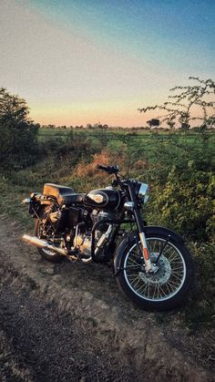 a motorcycle parked on the side of a dirt road next to a lush green field