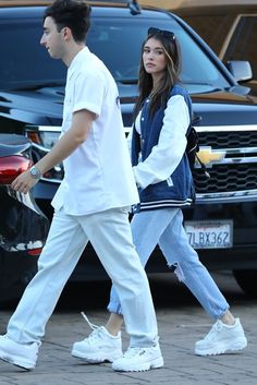 a man and woman are walking down the street with cars in the backgroud