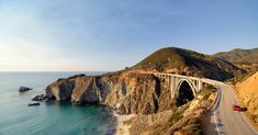 an aerial view of a highway going over the ocean with a bridge in the background