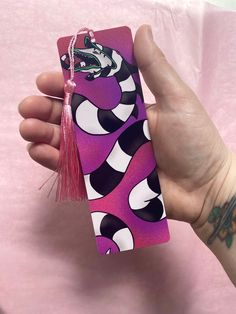 a hand holding a purple and black cell phone case with a tassel on it