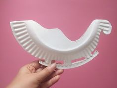 a hand holding a white paper plate shaped like a toothbrush holder against a pink background