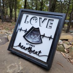 a sign that says love is in the middle of some rocks with trees in the background