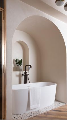 a large white bath tub sitting next to a wooden floor in a bathroom with an arched wall