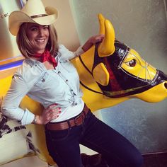 a woman wearing a cowboy hat poses next to a yellow cow statue with her hands on her hips