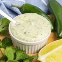 a small white bowl filled with green sauce next to sliced limes and cilantro