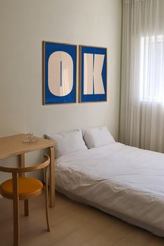 two paintings hang on the wall above a bed in a room with white sheets and pillows