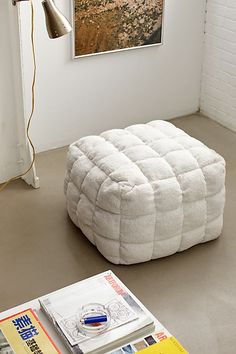 a large white ottoman sitting on top of a floor next to a lamp and books