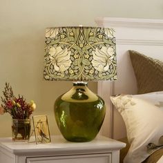 a green lamp sitting on top of a night stand next to a bed with pillows