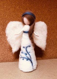 an angel figurine with long brown hair and white wings is posed against a wall