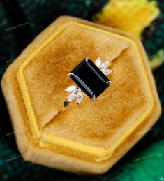 an engagement ring with black onyxite surrounded by yellow velvet and diamond accents, in front of a green background