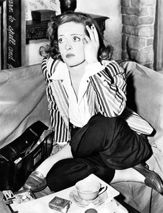 a black and white photo of a woman sitting on a couch holding her hand to her head