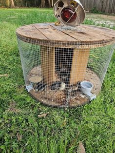 a caged in bird feeder with two birds inside it on the grass next to a fence