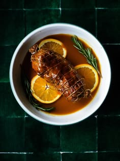 a white bowl filled with meat and oranges on top of a green tablecloth