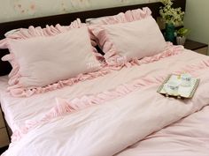 a bed with pink ruffled sheets and pillows on it, next to a vase