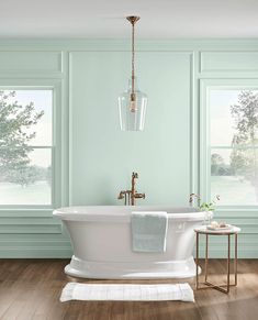 a white bath tub sitting in a bathroom next to two windows and a wooden floor