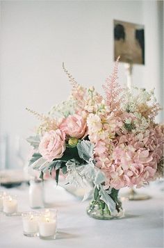 a vase filled with lots of pink flowers on top of a white table covered in candles