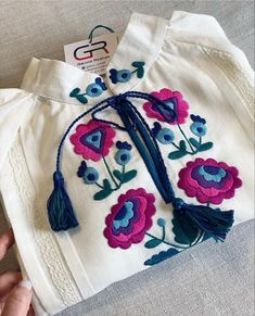 a hand embroidered shirt with flowers and tassels is being held up by someone