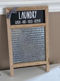 a sign that is sitting on top of a shelf in front of a window with the words laundry wash dry fold - repeat