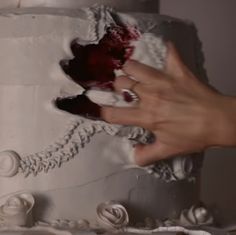 two hands are decorating a wedding cake with white frosting and red flowers on it