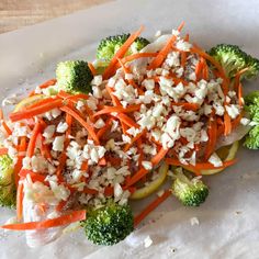 a white plate topped with broccoli, carrots and other food on top of paper