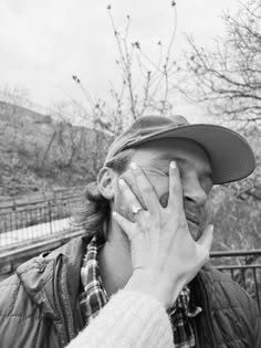 a man holding his hand up to his face while standing in front of a fence