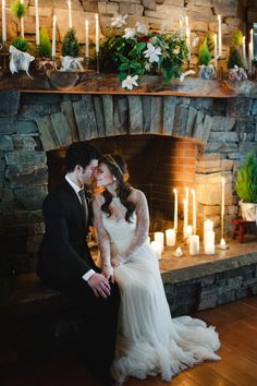 a bride and groom sitting in front of a fire place with candles on the mantle