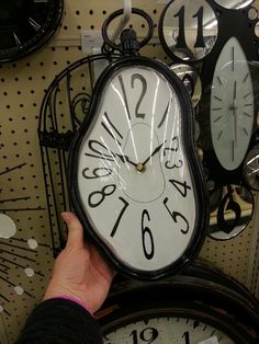 a person holding up a clock in front of several clocks