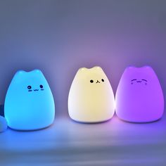 three different colored lights that look like cats with eyes and noses on them, sitting in front of a gray background