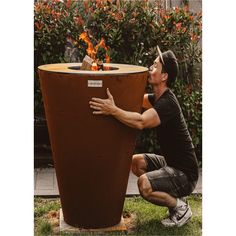 a man kneeling down next to a large pot with fire in it's center