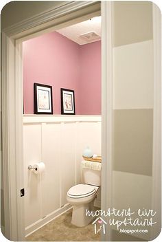 a white toilet sitting in a bathroom next to a pink wall with two pictures on it