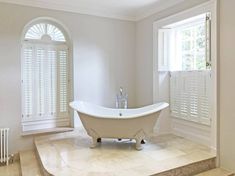 a white bath tub sitting in the middle of a bathroom next to a window with shutters